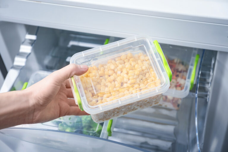 a person holding a container of food in front of an open refrigerator.