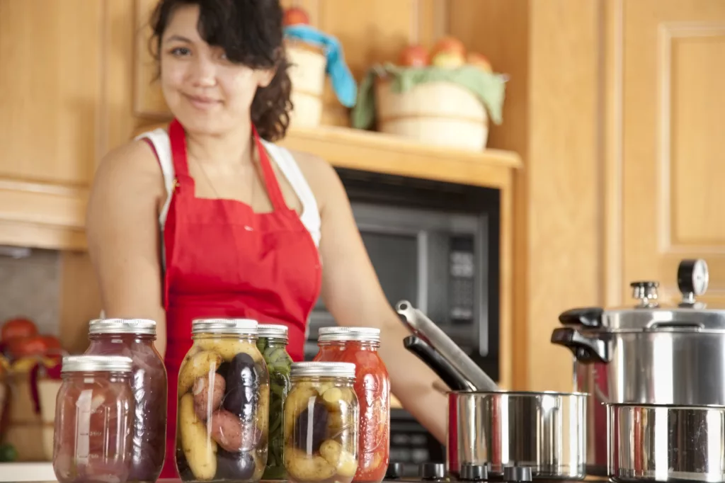 A waist up image of a mixed race (Caucasian, Asian, Pacific Islander) young adult woman canning homegrown fruits and vegetables.
