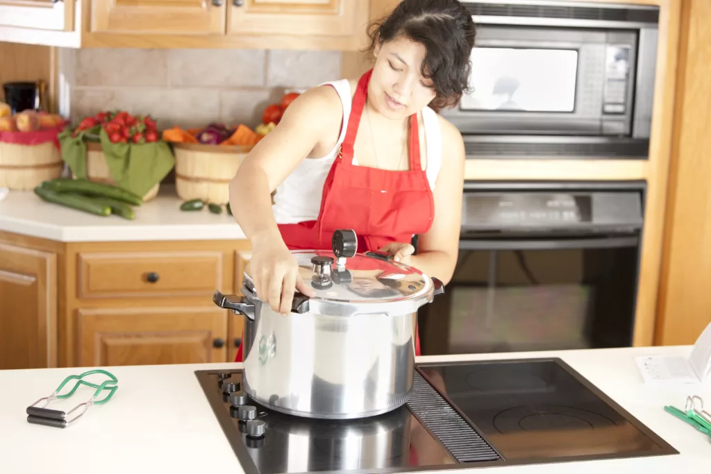 A waist up image of a mixed race (Caucasian, Asian, Pacific Islander) young adult woman canning homegrown fruits and vegetables.