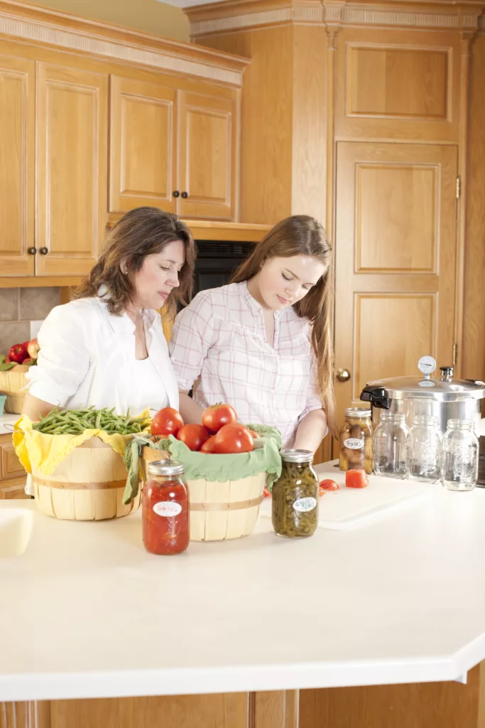 A waist up image of a caucasian mother and teenage daughter canning homegrown fruits and vegetables.